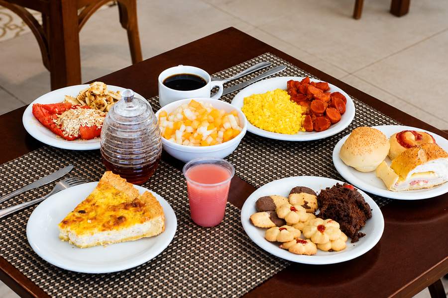 Mesa de café da manhã com café, frutas, ovos, quiche e pães frescos
